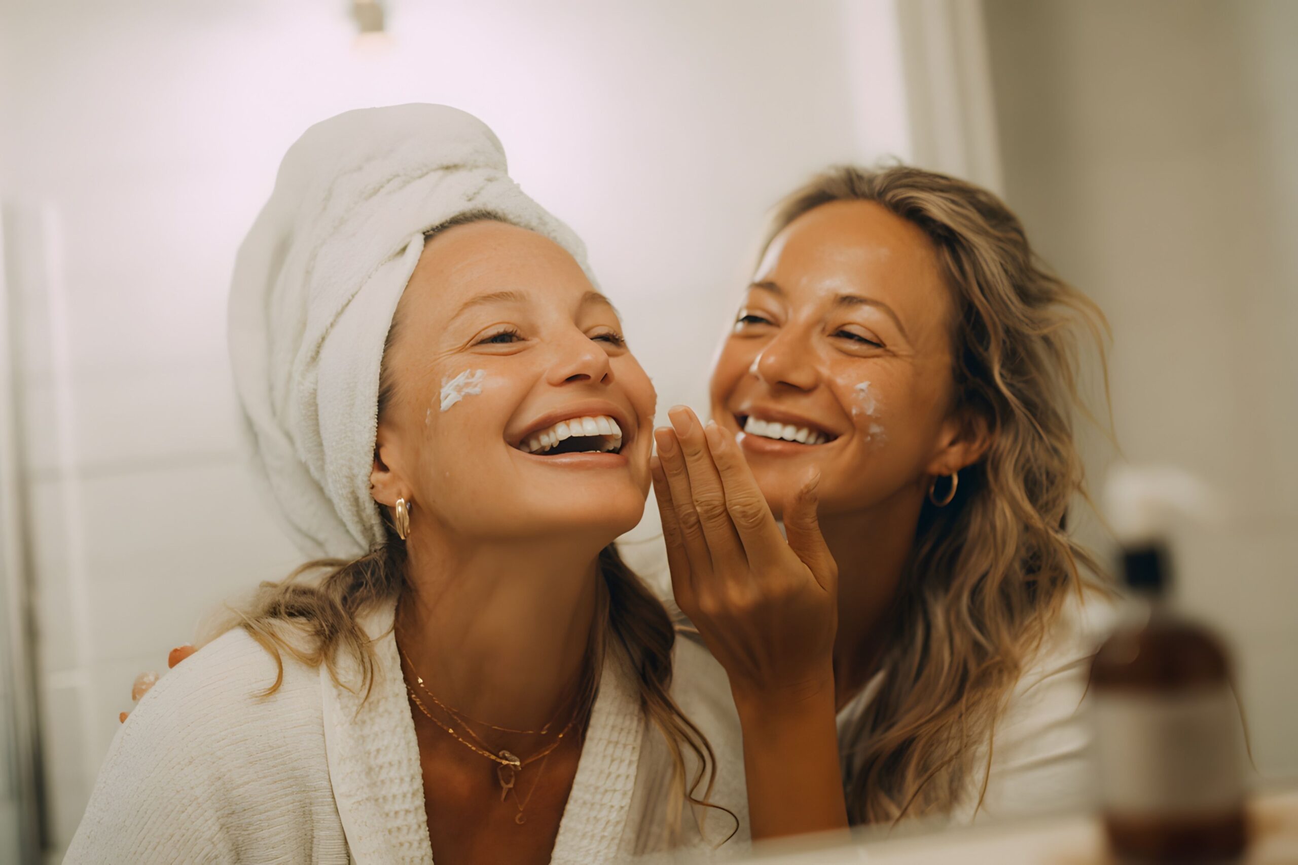 Two young European women applying cold weather skincare moisturizer during winter morning routine with natural window lighting