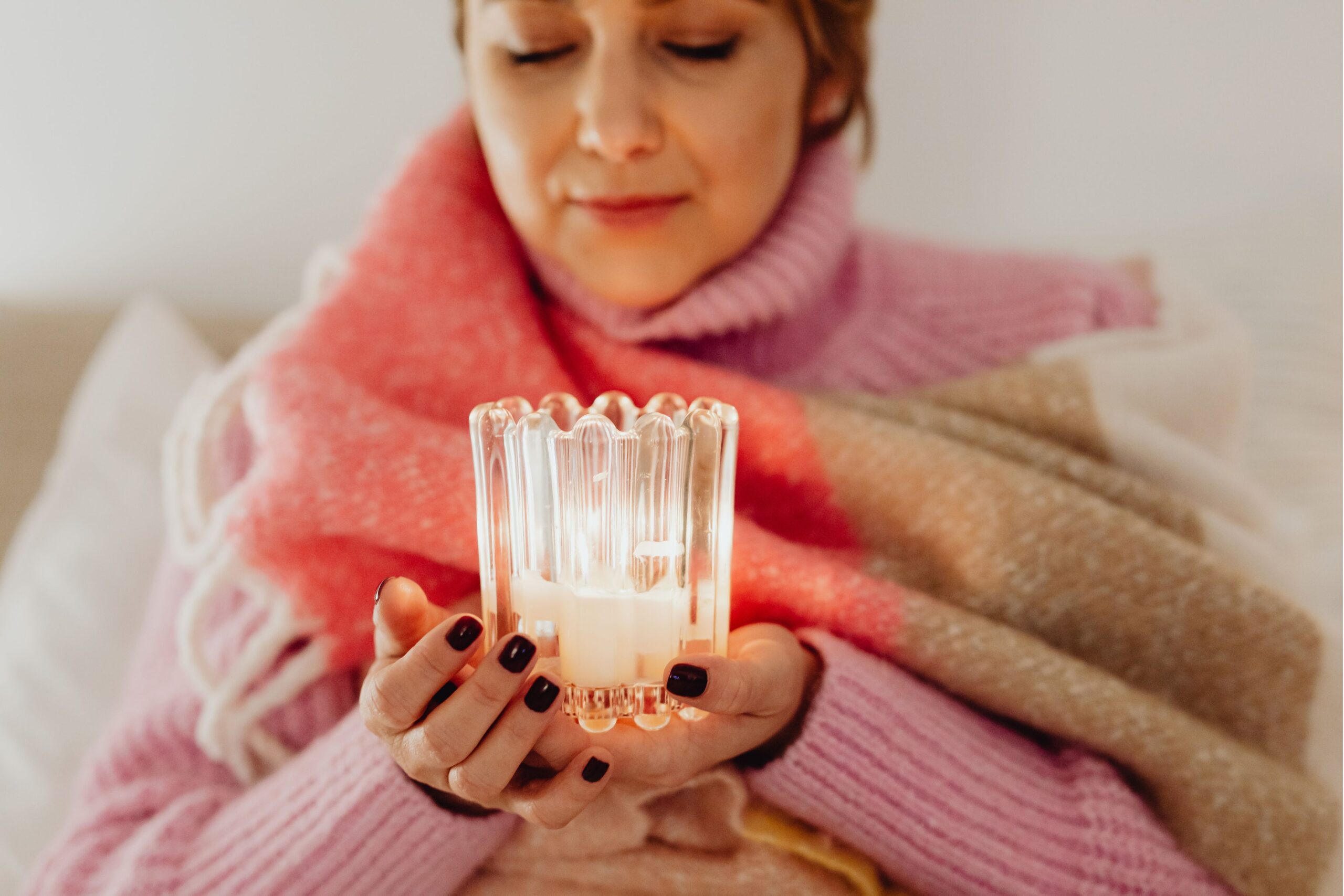 Woman enjoying winter wellness with candles in Danish hygge style interior featuring warm lighting and cozy textiles