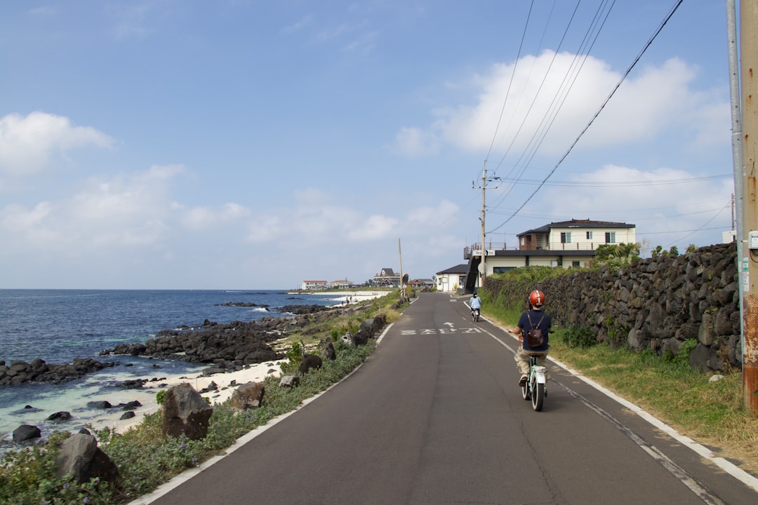 A cyclist on a certified EU coastal cycling route rides along a cliff-top path with the sea visible below