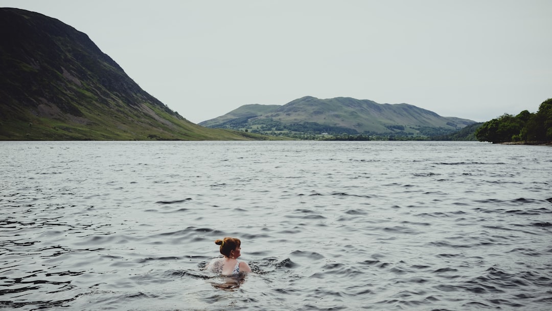 A swimmer wading into a certified EU open-water lake on a clear summer morning, with safety buoys visible in the background.