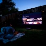 A crowd of people seated on a summer evening watching an open-air cinema screening at a European festival