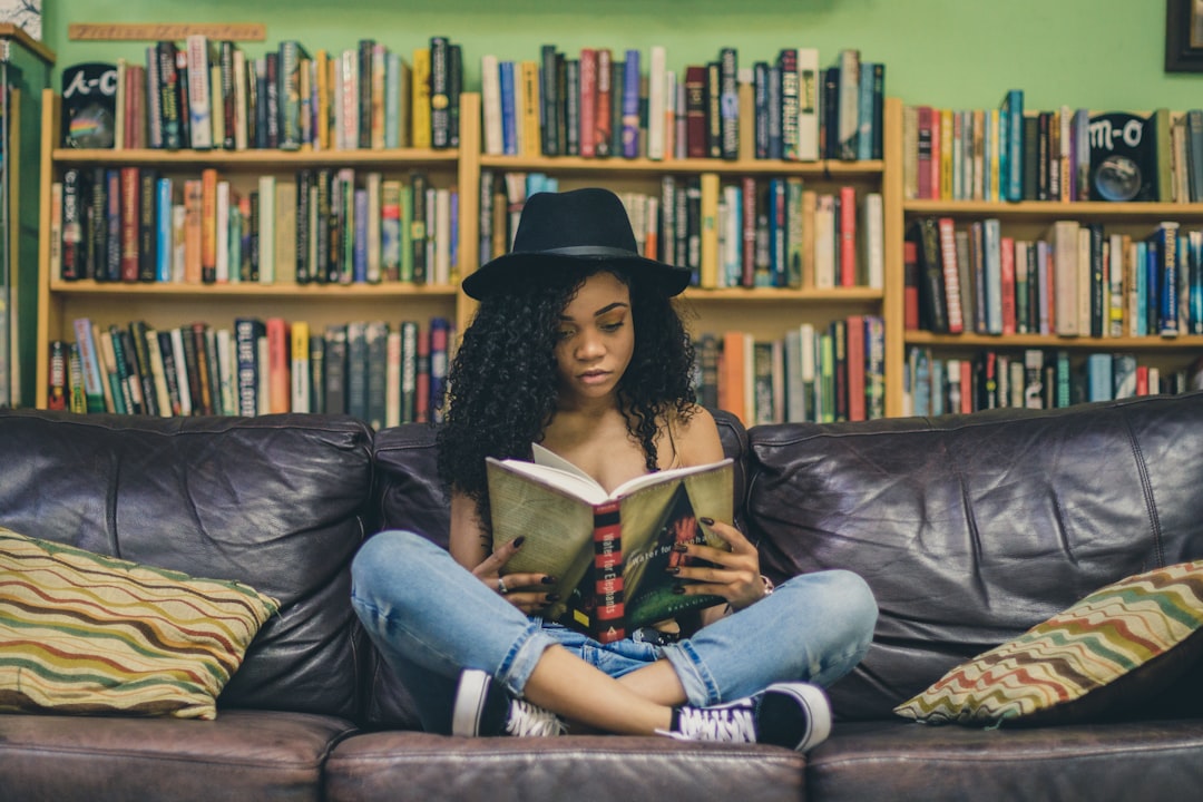 A woman reads a minority language poetry collection in a European library, surrounded by shelves of multilingual literary.