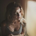 A woman standing by a bright window in autumn morning light, actively resetting her daily rhythm with natural light exposure.