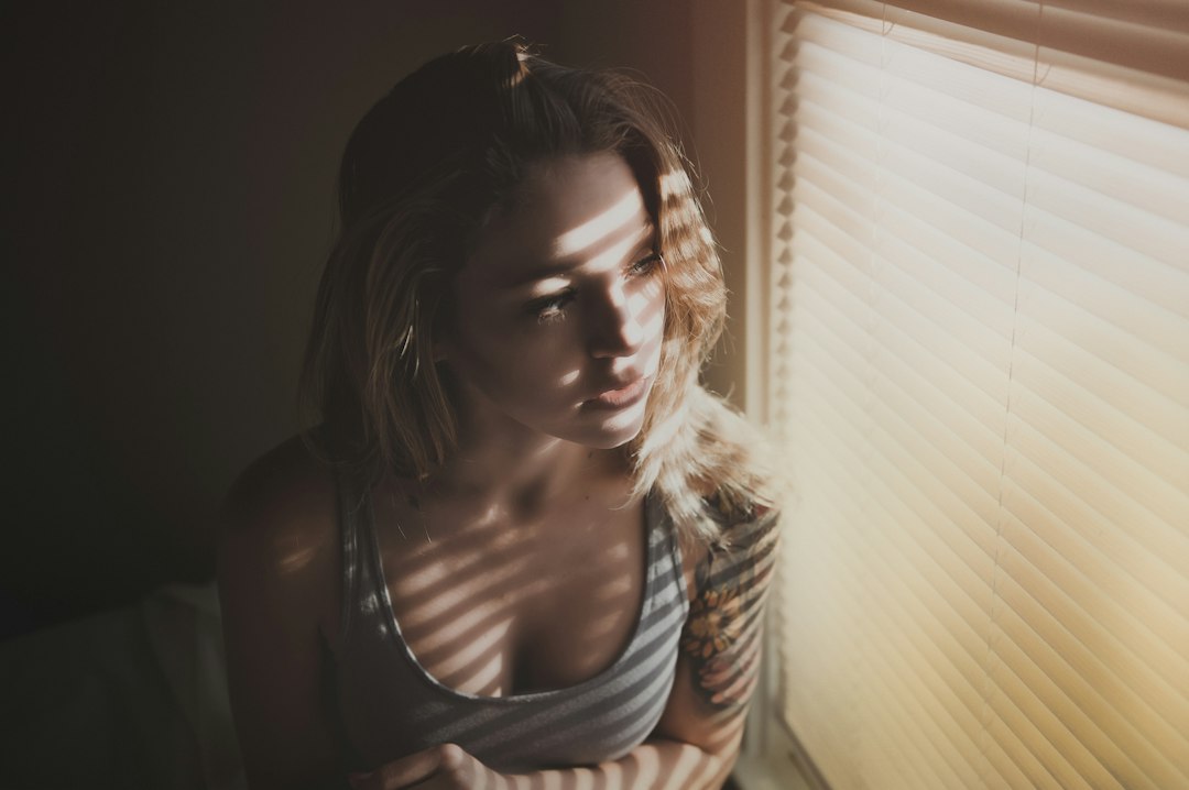 A woman standing by a bright window in autumn morning light, actively resetting her daily rhythm with natural light exposure.